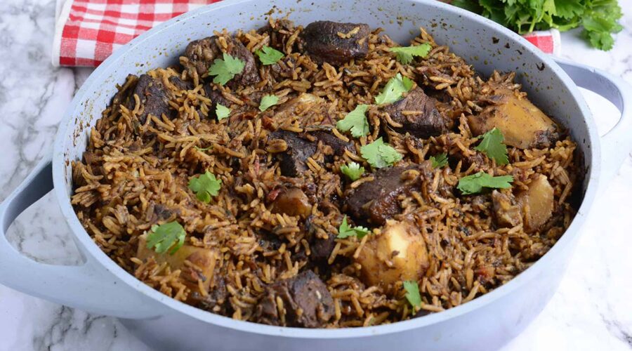 Kenyan pilau with meat and potatoes, garnished with cilantro served in a white pot.
