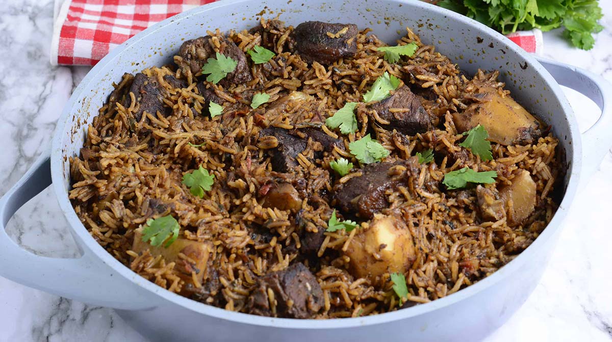 Kenyan pilau with meat and potatoes, garnished with cilantro served in a white pot.