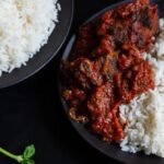 Nigerian tomato stew with goat meat served on a plate with white rice.