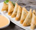 Samosas served on a white plate with cilantro garnish and a creamy sauce.