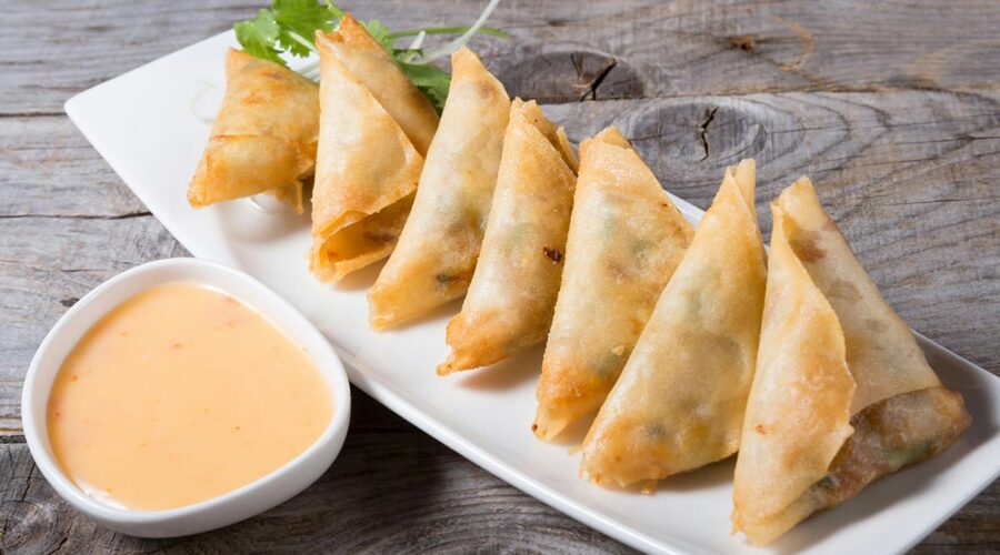 Samosas served on a white plate with cilantro garnish and a creamy sauce.