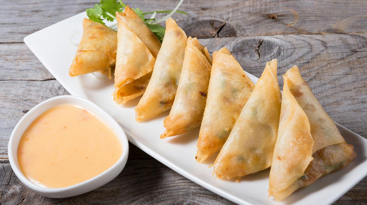 Samosas served on a white plate with cilantro garnish and a creamy sauce.