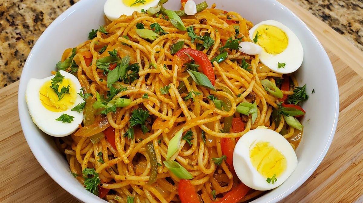 A plate of Haitian smoked herring and spaghetti served with boiled eggs and garnished with scallions and cilantro