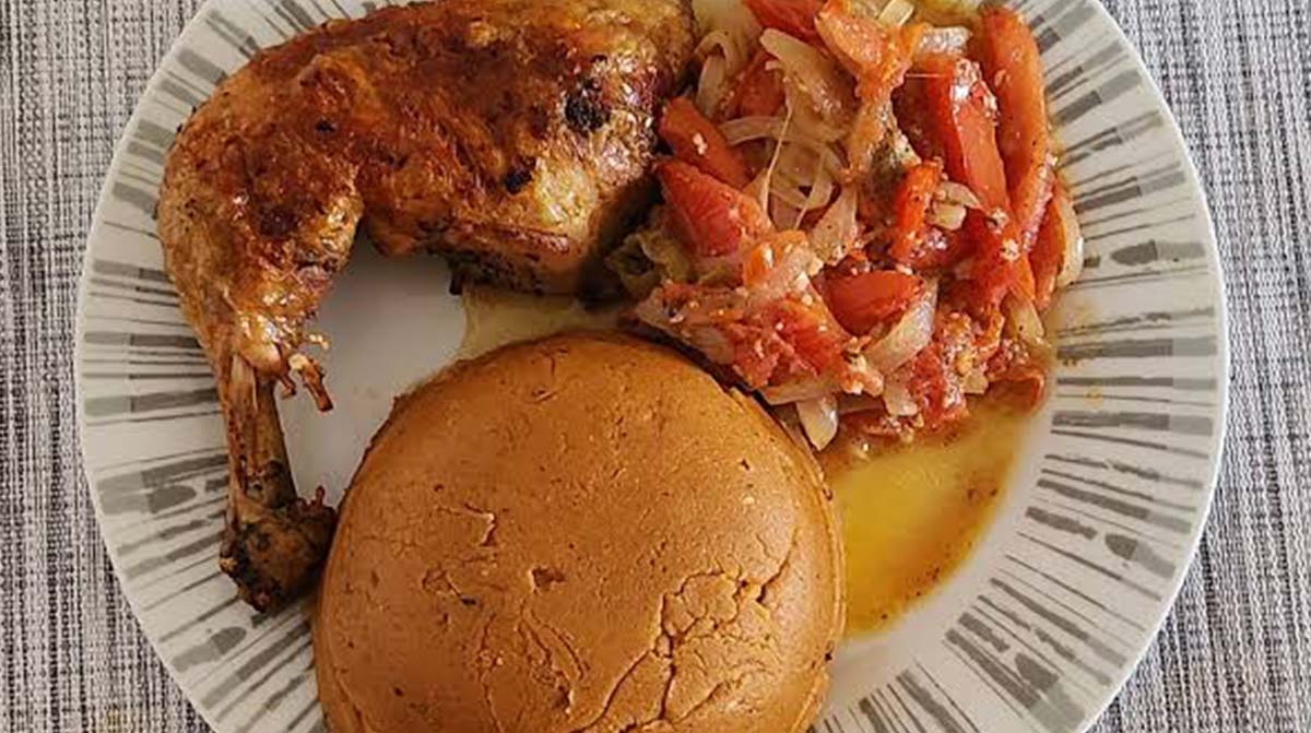 Beninese amiwo tomato cornmeal served with browned chicken and onions on a white plate