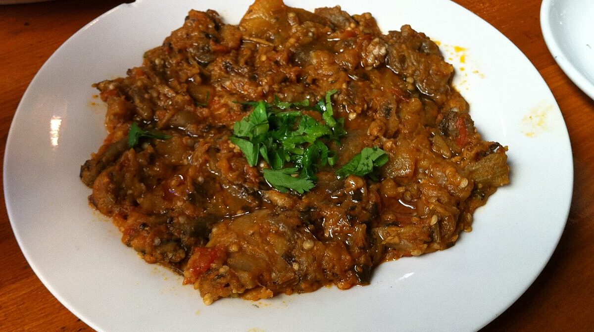 Moroccan zaalouk cooked eggplant and tomato salad garnished with herbs on a white plate