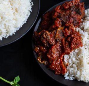 Nigerian tomato stew with goat meat served on a plate with white rice.